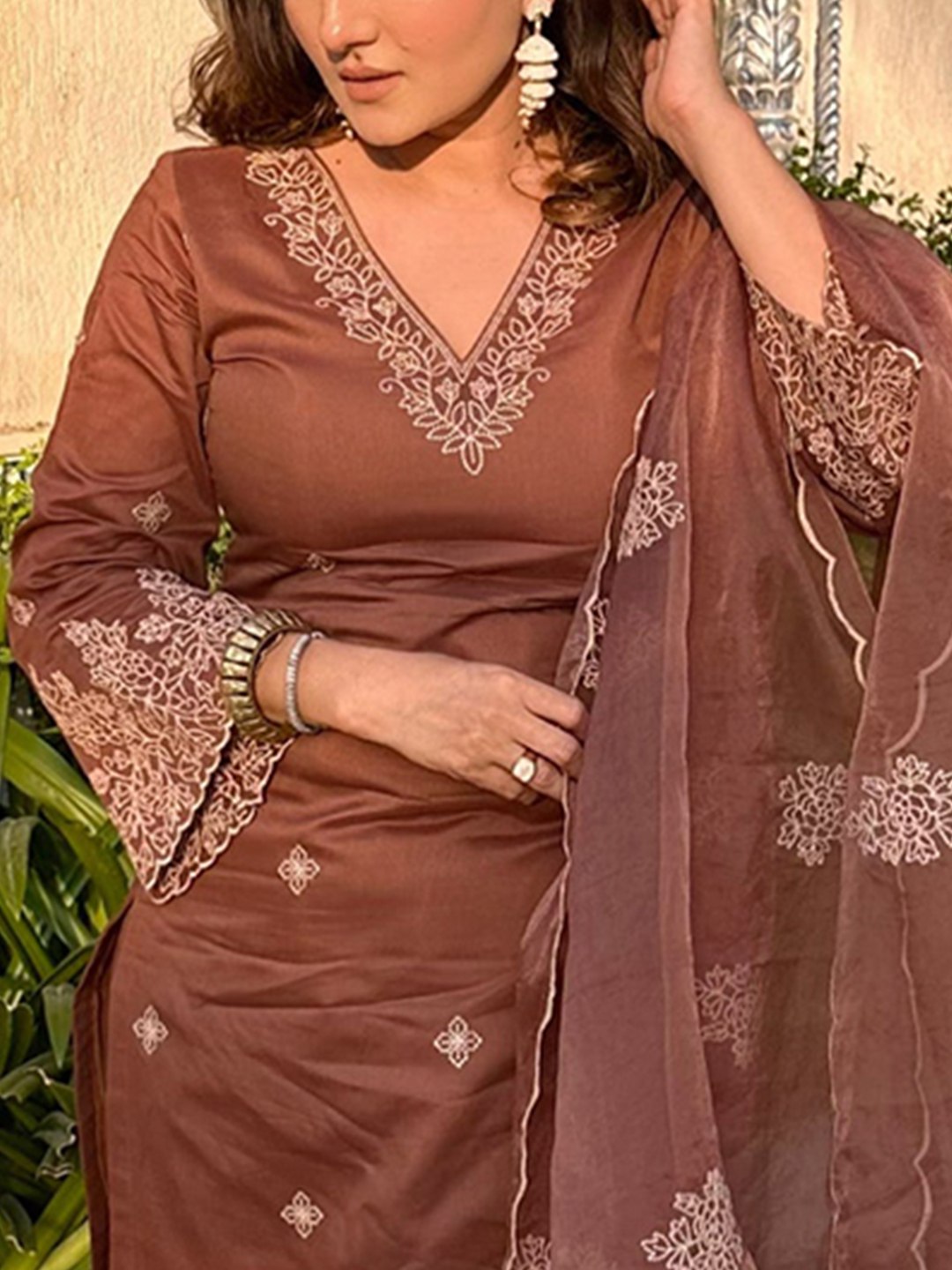 Woman wearing a chocolate brown silk blend kurta set with intricate zari embroidery on the neckline and bell sleeves, paired with matching pants.
