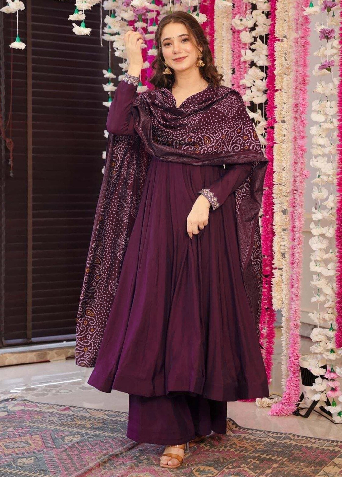 Woman wearing a deep purple flared anarkali kurta with full sleeves and subtle embellishments, paired with matching pants and a vibrant Bandhani print dupatta.