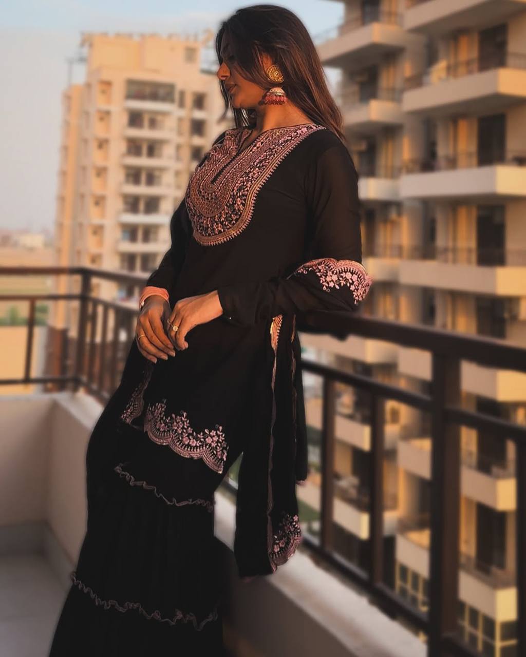 Designer black party wear gharara set for women, featuring a heavily embroidered kurta with contrast pink work and a voluminous tiered ruffled sharara.
