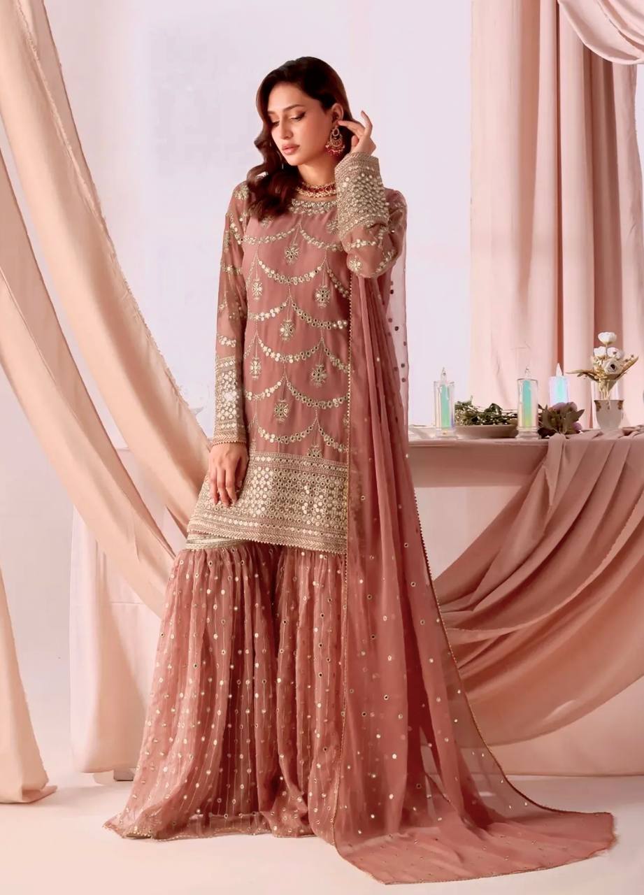 Woman wearing a dusty rose pink georgette kurta sharara suit with heavy gold sequin and zari embroidery on the kurta, full sleeves, and tiered sharara, with a matching sheer dupatta.