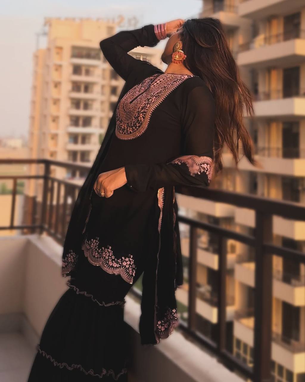 Elegant black ethnic wear featuring a mid-length kurta with intricate contrast pink embroidery and a matching layered ruffled sharara, perfect for special occasions.
