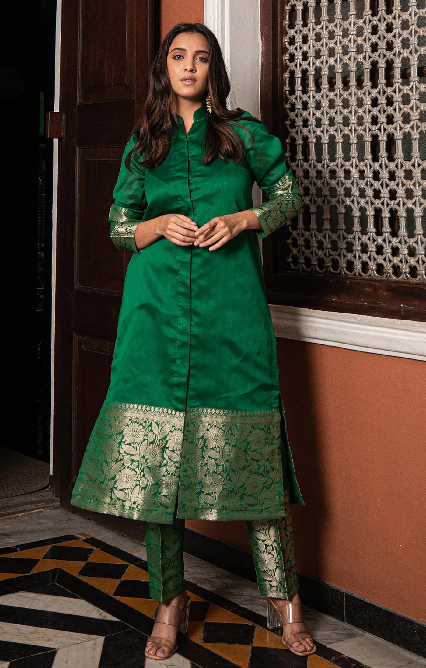 Woman wearing an emerald green silk blend kurta with gold brocade work on sleeves and hem, paired with matching straight pants.