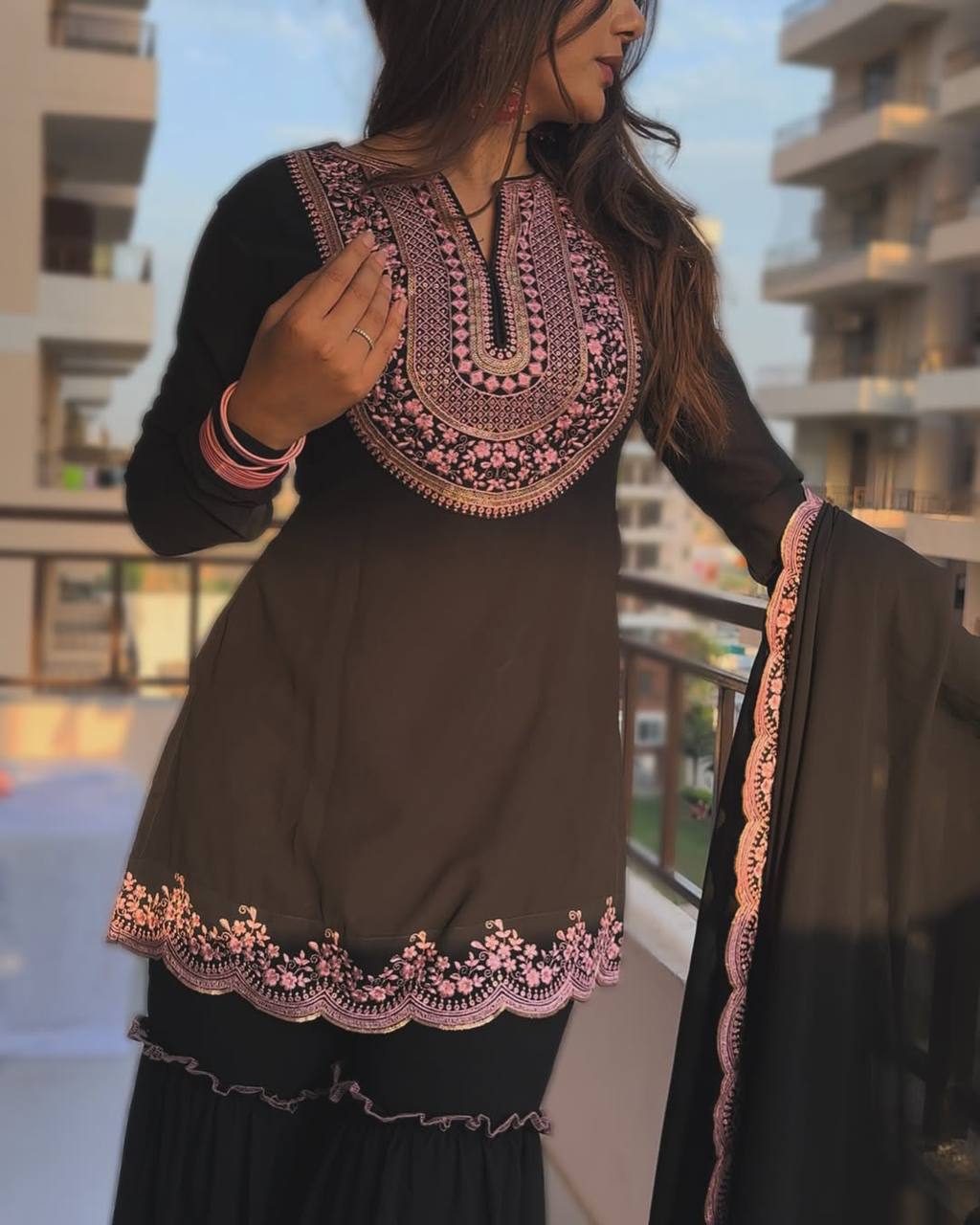 Model in an elegant evening wear black sharara suit with long sleeves, intricate rose gold embroidery on the kurta, and a stylish ruffled tiered sharara.