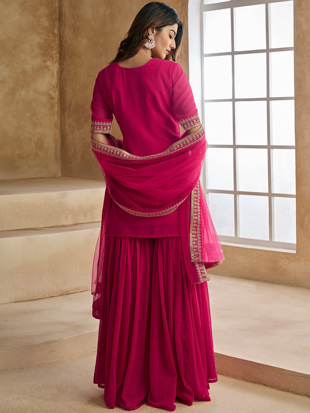 Model in a festive rani pink sharara suit, perfect for Sangeet and Mehendi functions, with intricate gold thread work.
