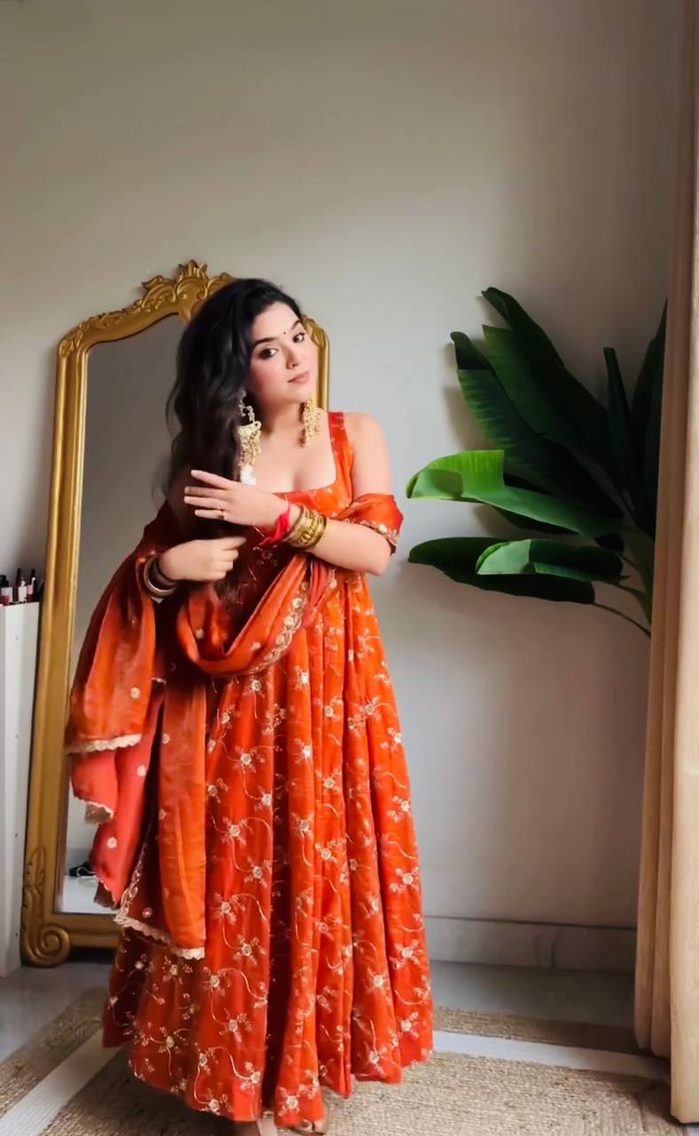 Model in a Haldi special orange anarkali gown with intricate gold floral patterns, a strappy neckline, and a flowing dupatta, perfect for pre-wedding functions.