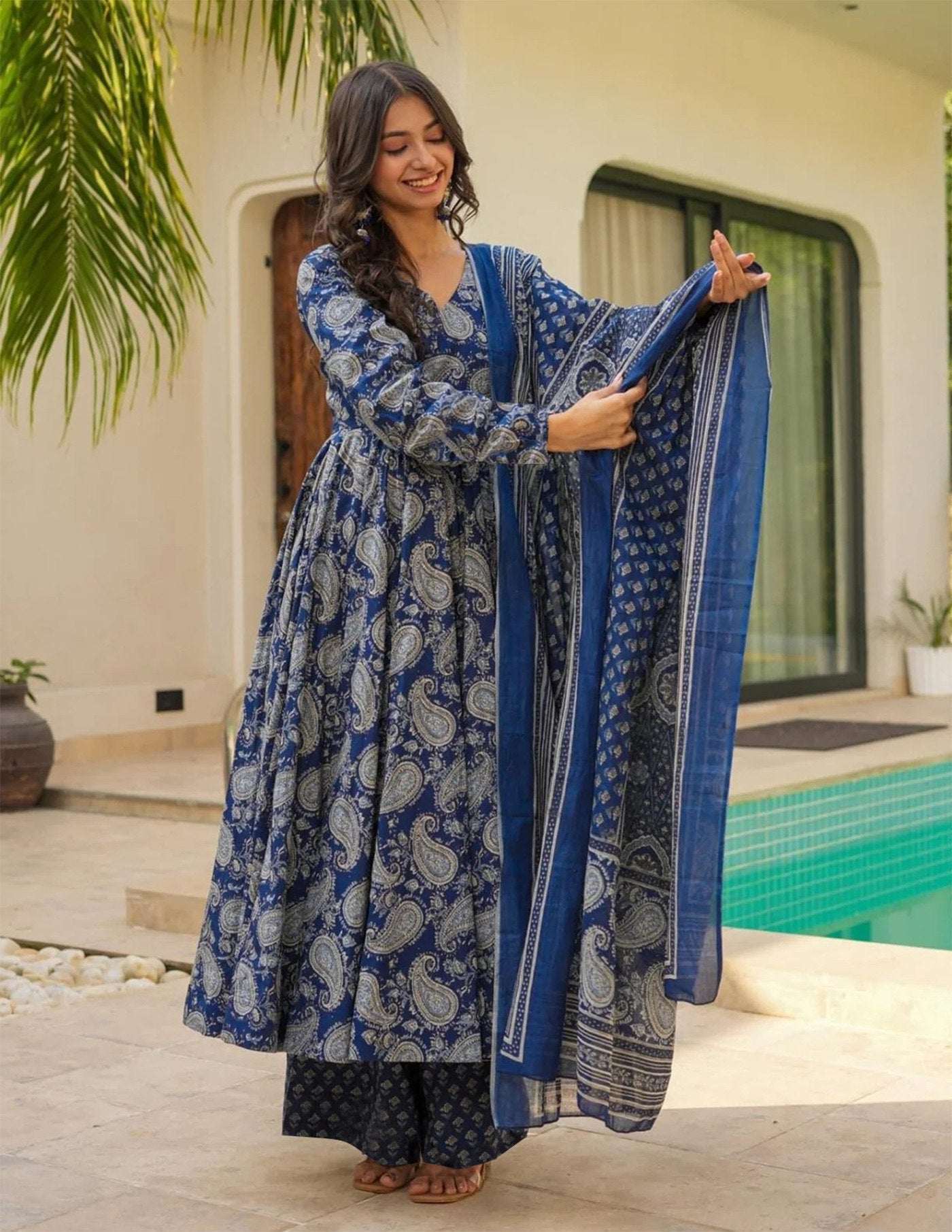 Woman wearing indigo blue cotton anarkali kurta set with paisley block prints, matching palazzo, and dupatta.
