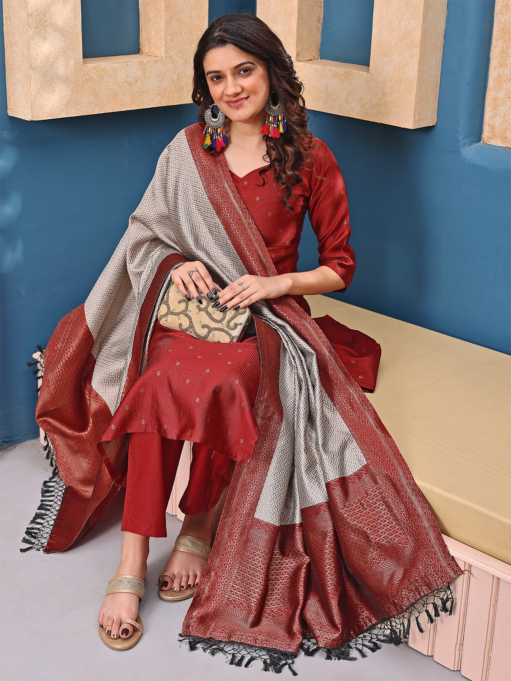 Woman wearing a maroon silk blend kurta set with straight pants and a striking grey and silver woven dupatta with tassels.