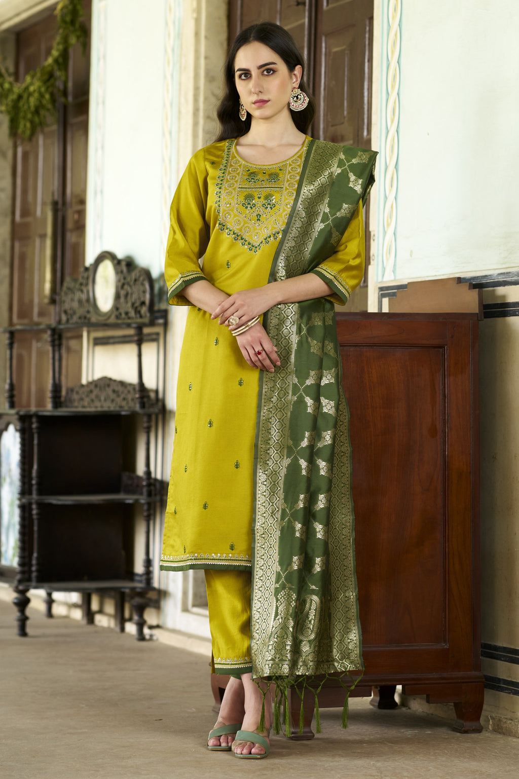 Woman wearing a mustard yellow silk blend kurta set with embroidered yoke, straight pants, and a rich bottle green Banarasi dupatta.