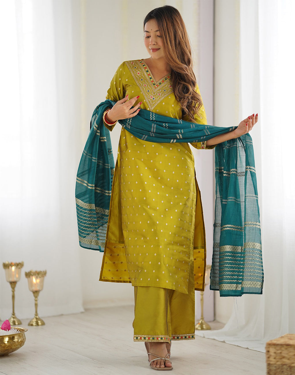 Woman wearing a vibrant mustard yellow silk blend kurta set with embroidered neckline and a contrasting teal dupatta.