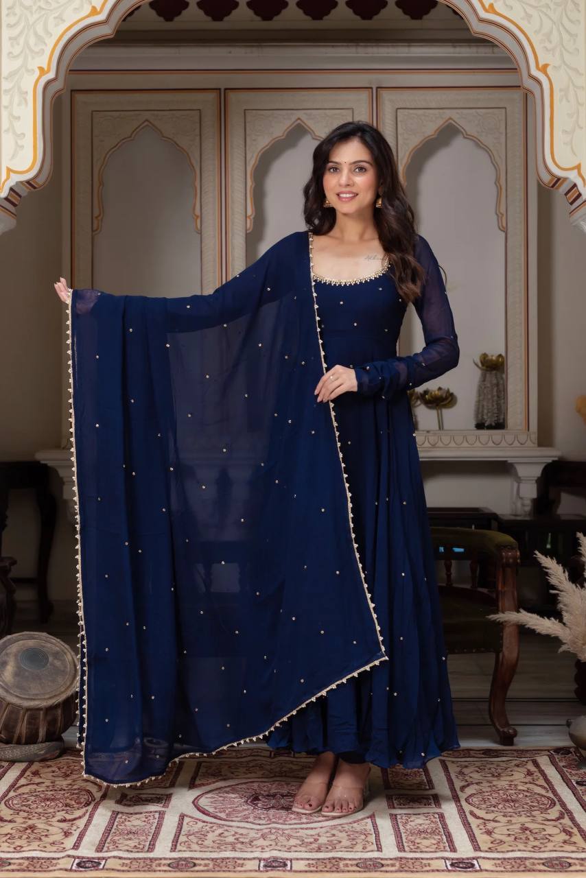 Woman wearing an elegant navy blue georgette anarkali gown with a round neckline adorned with gold lace, full sleeves, a generous flare, and a matching dupatta with gold bootis and border.