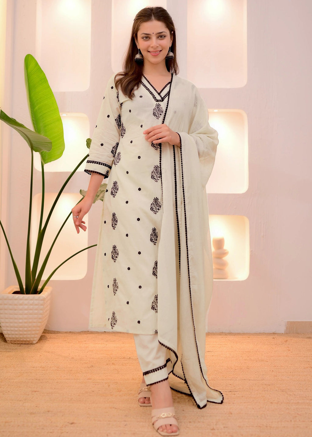 Woman wearing an off-white cotton kurta set with black embroidered floral motifs and black lace trim on the neckline, sleeves, and pants.