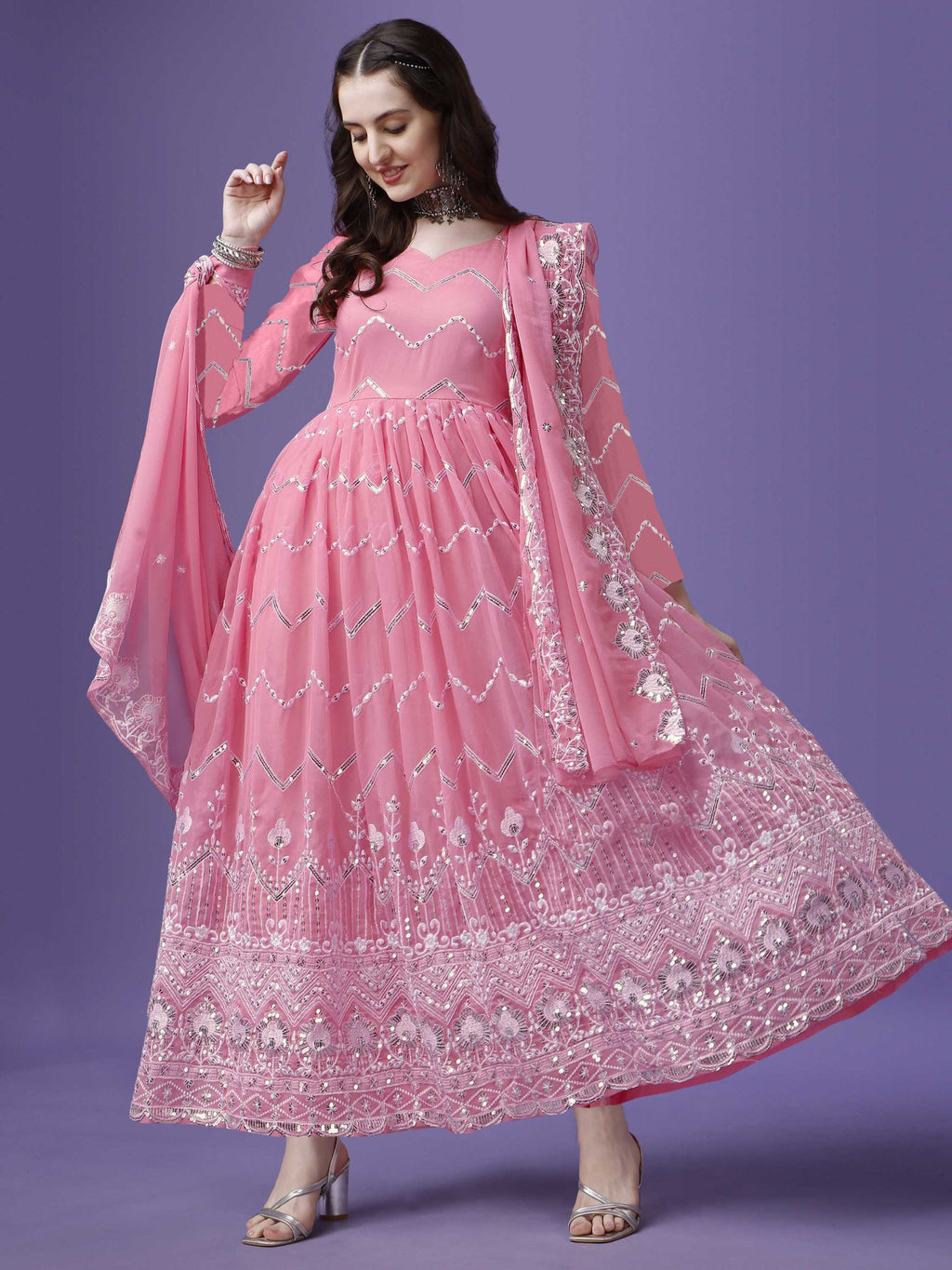 Woman wearing a flowing pink georgette anarkali gown with intricate silver zari and sequin embroidery on the bodice and flared hem, paired with a matching dupatta.

