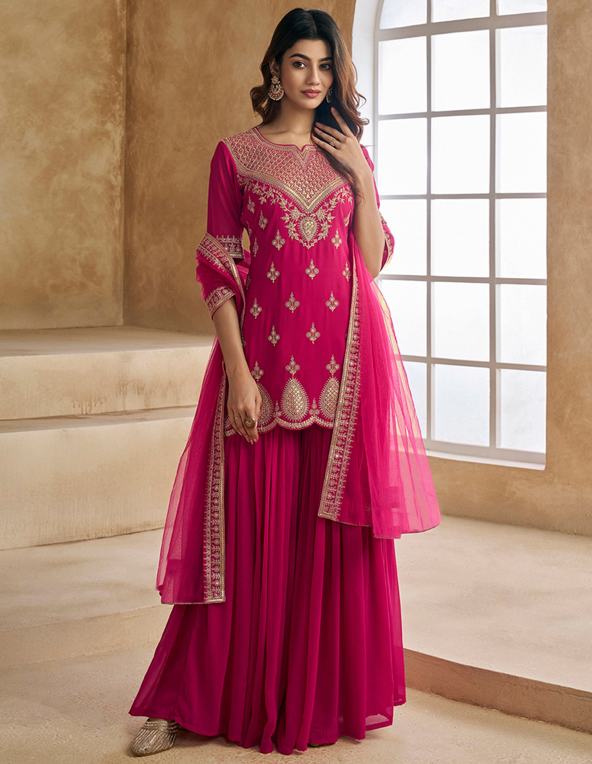 Woman wearing a vibrant rani pink georgette sharara suit with intricate gold zari and thread embroidery on the kurta and sharara hem, paired with a matching dupatta.