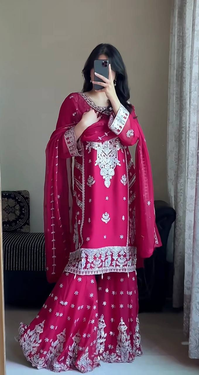 Woman wearing a vibrant rani pink georgette kurta gharara suit with heavy silver zari and sequin embroidery on the kurta, full sleeves, and tiered gharara, with a matching sheer dupatta.