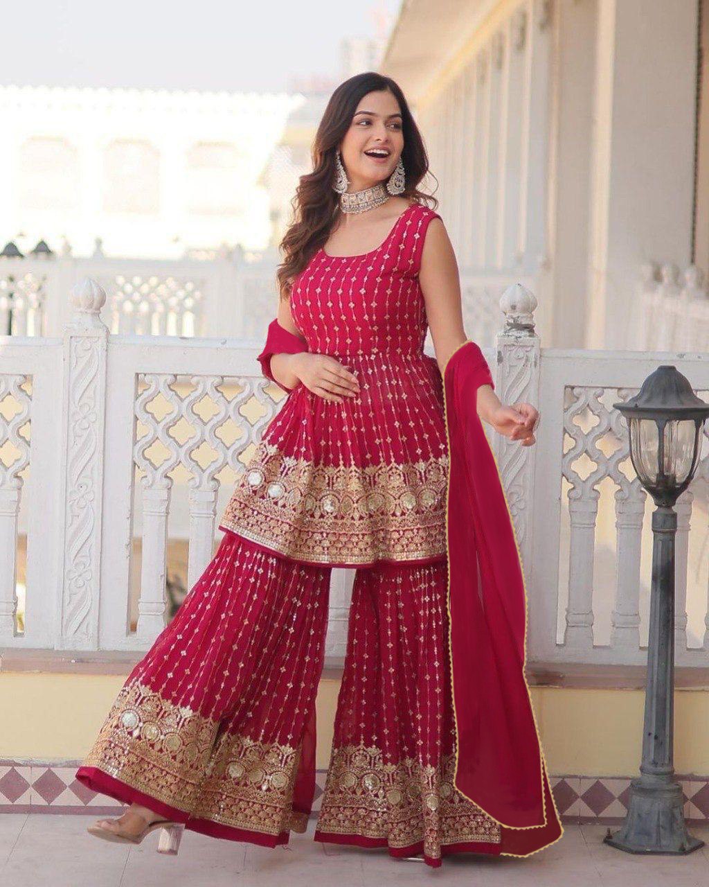 Woman wearing a vibrant rani pink peplum style short kurta with intricate gold gota patti and mirror work, paired with a voluminous embroidered sharara and matching dupatta.
