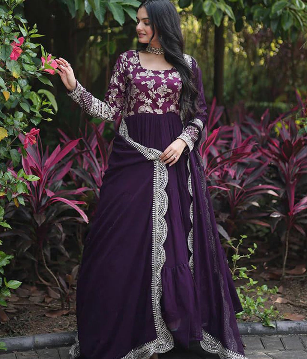 Woman wearing a royal purple georgette tiered anarkali gown with heavy gold zari embroidery on the bodice and sleeves, paired with a matching scalloped dupatta.