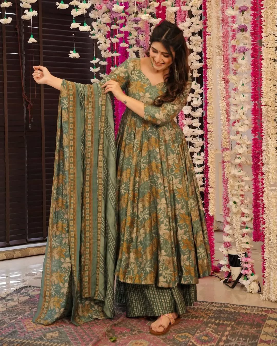 Woman wearing a sage green floral printed anarkali kurta set with matching palazzo pants and dupatta.
