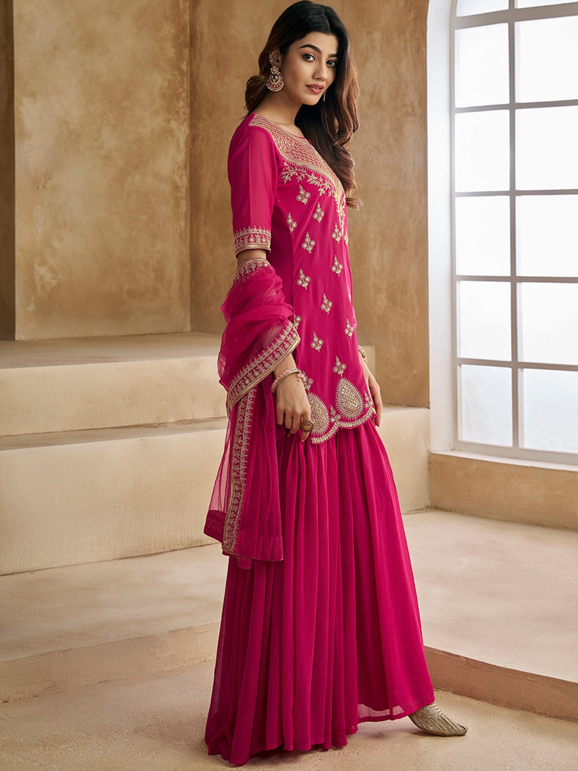 Traditional rani pink sharara suit with a short embroidered kurta, flared sharara pants, and a net dupatta.